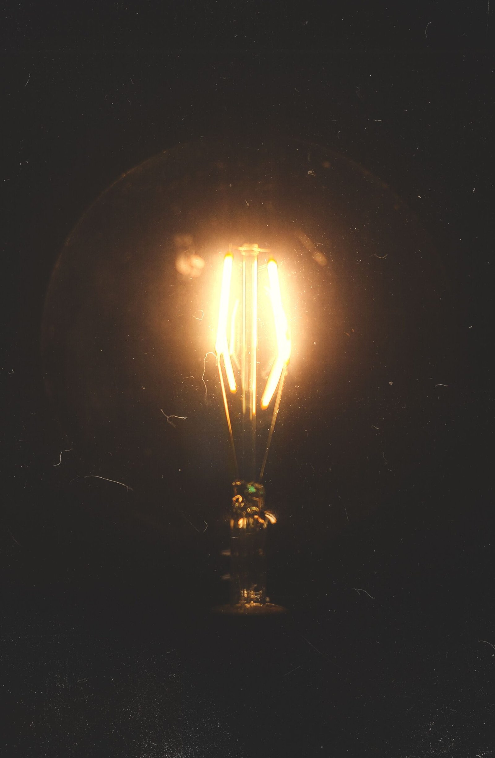 A close-up view of an incandescent light bulb glowing warmly in the dark, creating a moody atmosphere.